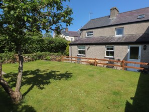 A two-story house with a stone facade, a wooden fence, and a grassy yard. - Bwthyn Defaid (Pwllheli)