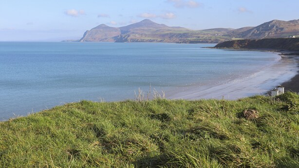 A coastal landscape with a grassy foreground, a calm sea, and distant mountains. - Bwthyn Defaid (Pwllheli)