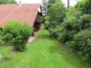 Situated in a lush garden, this traditional house features a wooden porch and a well-maintained garden path with a variety of plants and flowers.