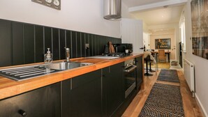 Una cocina moderna con encimera de madera, pileta de acero inoxidable y muebles de cocina negros. Hay una cafetera y un hervidor en la encimera.