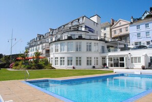 A white building with balconies and a swimming pool in front.