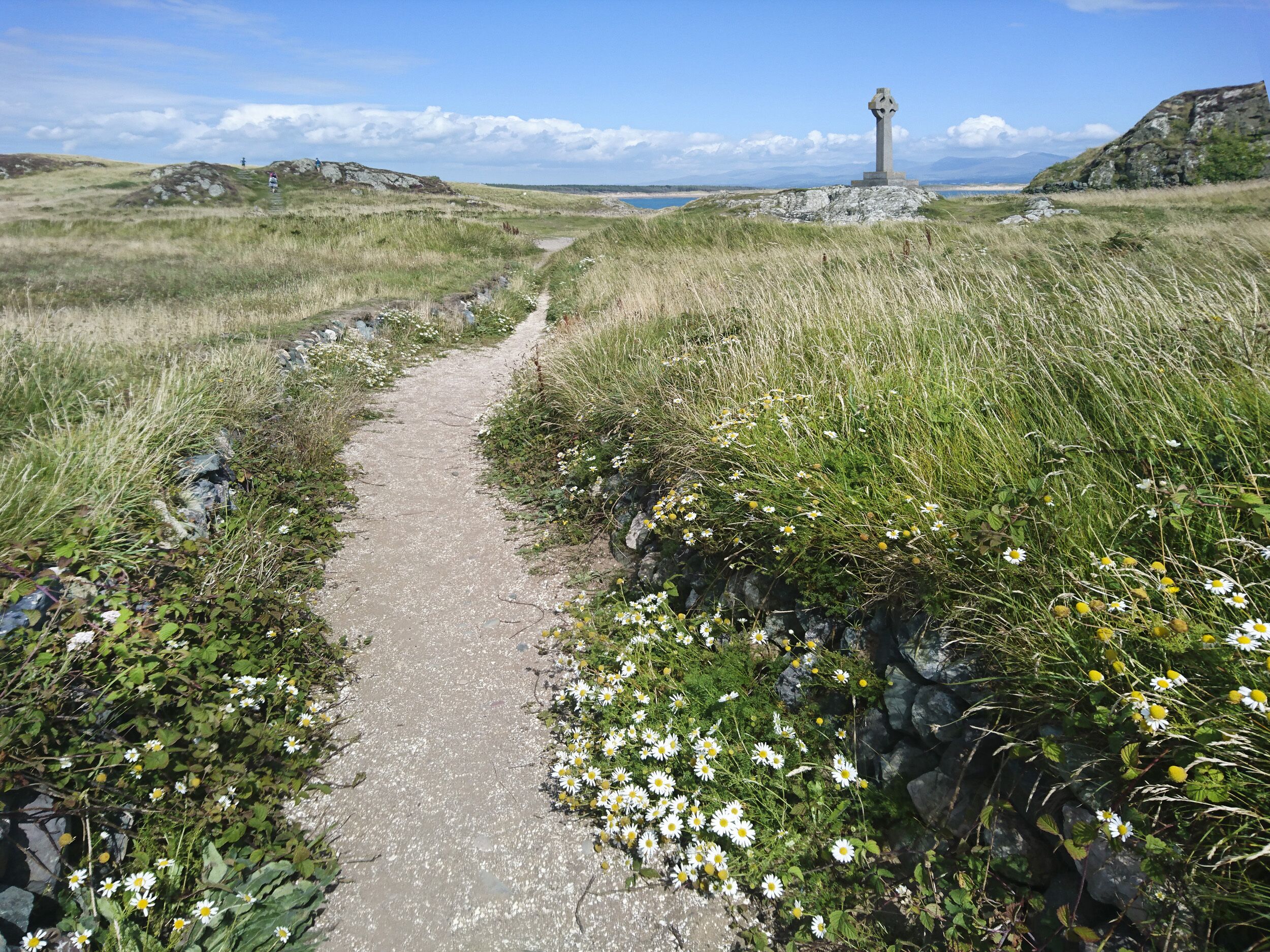 Un sentier étroit et non pavé mène à un monument de pierre situé dans un paysage verdoyant.