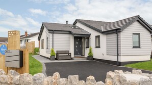 Une maison de campagne moderne à deux étages, avec une porte d’entrée sombre, un petit porche et un banc.