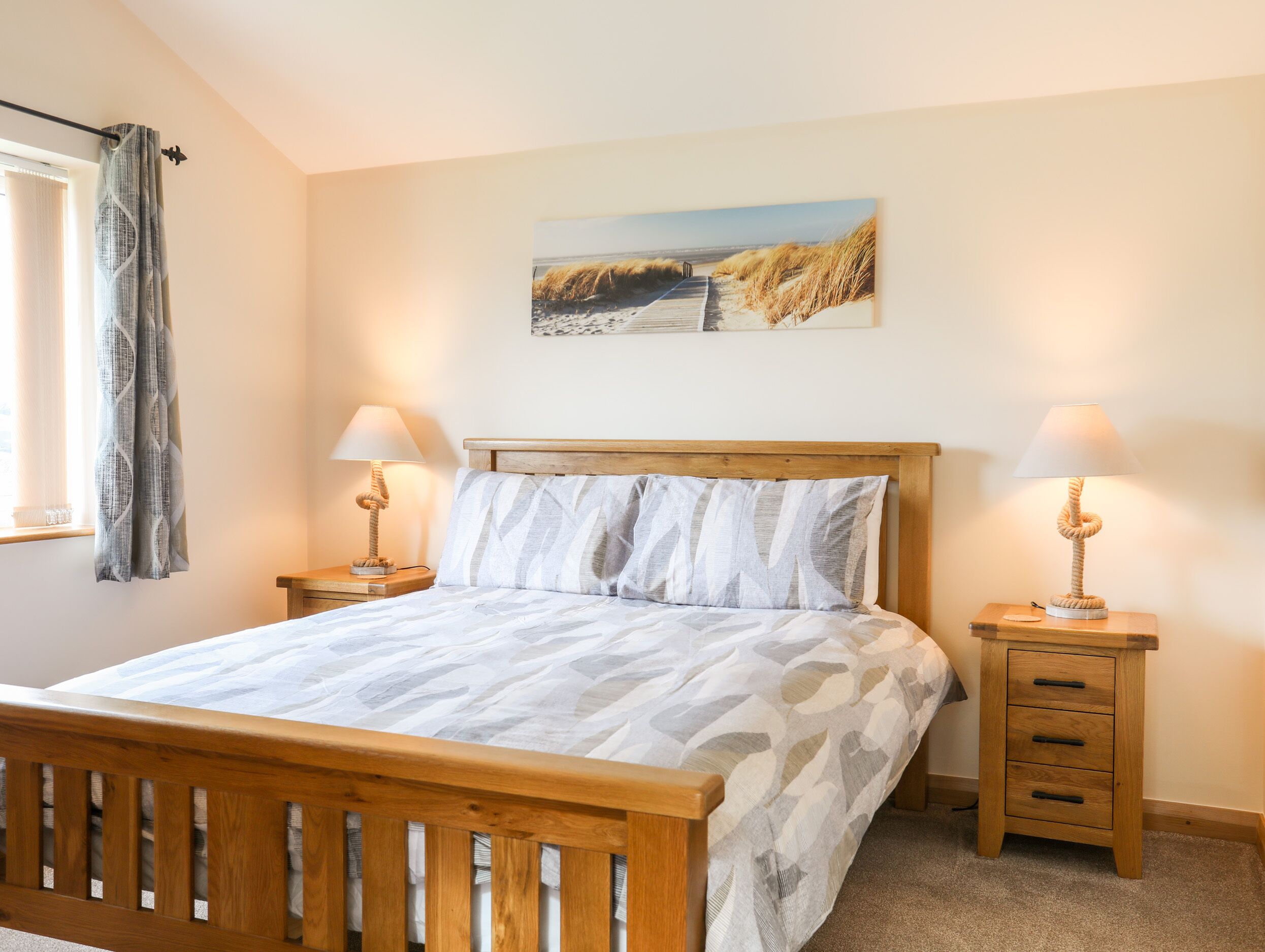 Een slaapkamer met een houten bed, twee nachtkastjes met lampen, een raam met gordijnen, en een schilderij aan de muur.