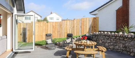 A patio area with a stone wall, wooden fence, and a round table with benches.