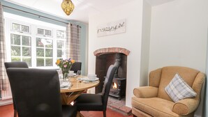 A cozy living room with a fireplace, a dining table with chairs, and a sofa with a plaid pillow. - Ryeby Garth (Hull)