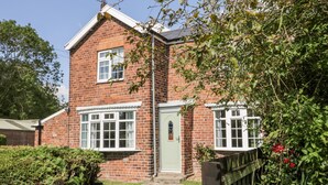 A two-story brick house with a green door, white-framed windows, and a small garden area with a wooden fence. - Ryeby Garth (Hull)