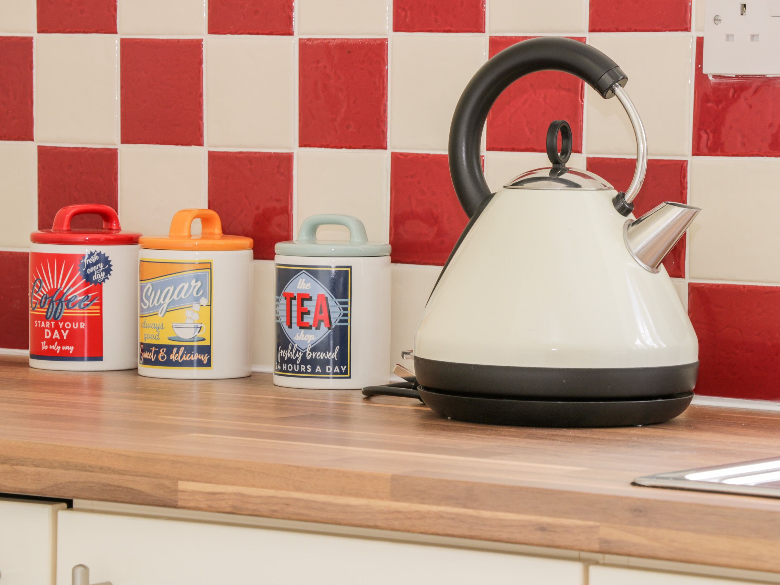 Una encimera de cocina con una tetera, un recipiente para café, un azucarero y un dispensador de té.