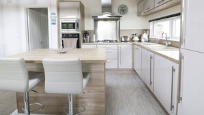 A modern kitchen with a wooden island, white bar stools, stainless steel appliances, and a window overlooking the garden. - 44 Heritage Park (Haverfordwest)