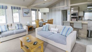 A spacious living area with two sofas, a coffee table, and a dining table. A kitchen area is visible in the background. - 44 Heritage Park (Haverfordwest)