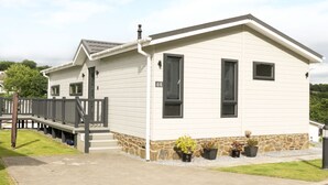 A single-story mobile home with a stone foundation, a covered porch, and a small garden with potted plants. - 44 Heritage Park (Haverfordwest)