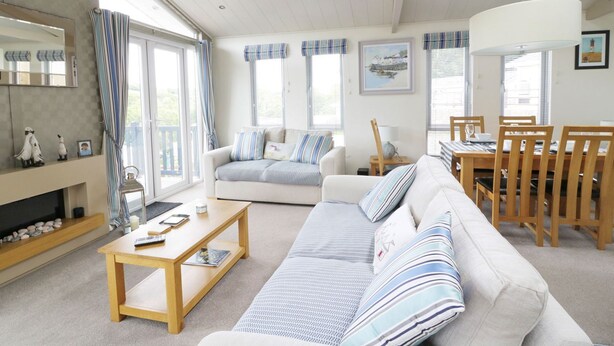 A well-lit living room with a sofa, coffee table, and dining area. - 44 Heritage Park (Haverfordwest)