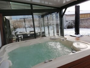 Ein Whirlpool mit Blick auf eine verschneite Winterlandschaft durch große Glasfenster.
