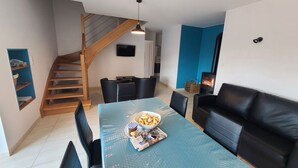 Un salon moderne avec un escalier en bois, une table à manger avec des magazines et des en-cas, un canapé en cuir noir et une cheminée.