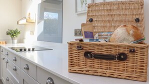 A kitchen with a modern design, featuring a white countertop, stainless steel appliances, and a wicker basket with bread and a coffee maker. - Ghyll Cottage (Milnthorpe)