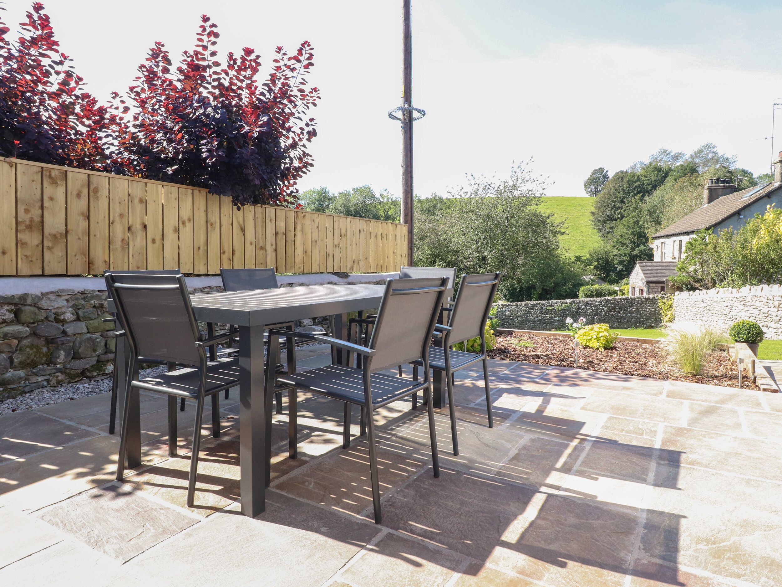 An outdoor patio with a table and chairs, a wooden fence, and a stone wall.