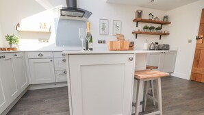 A modern kitchen with white cabinetry, a wooden bar stool, and a built-in stove. - Ghyll Cottage (Milnthorpe)