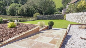 A landscaped garden with stone pathways, raised beds, and a variety of plants. - Ghyll Cottage (Milnthorpe)