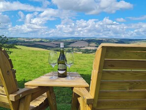 Un tavolo in legno con una bottiglia di vino e due bicchieri, sullo sfondo di un paesaggio rurale.