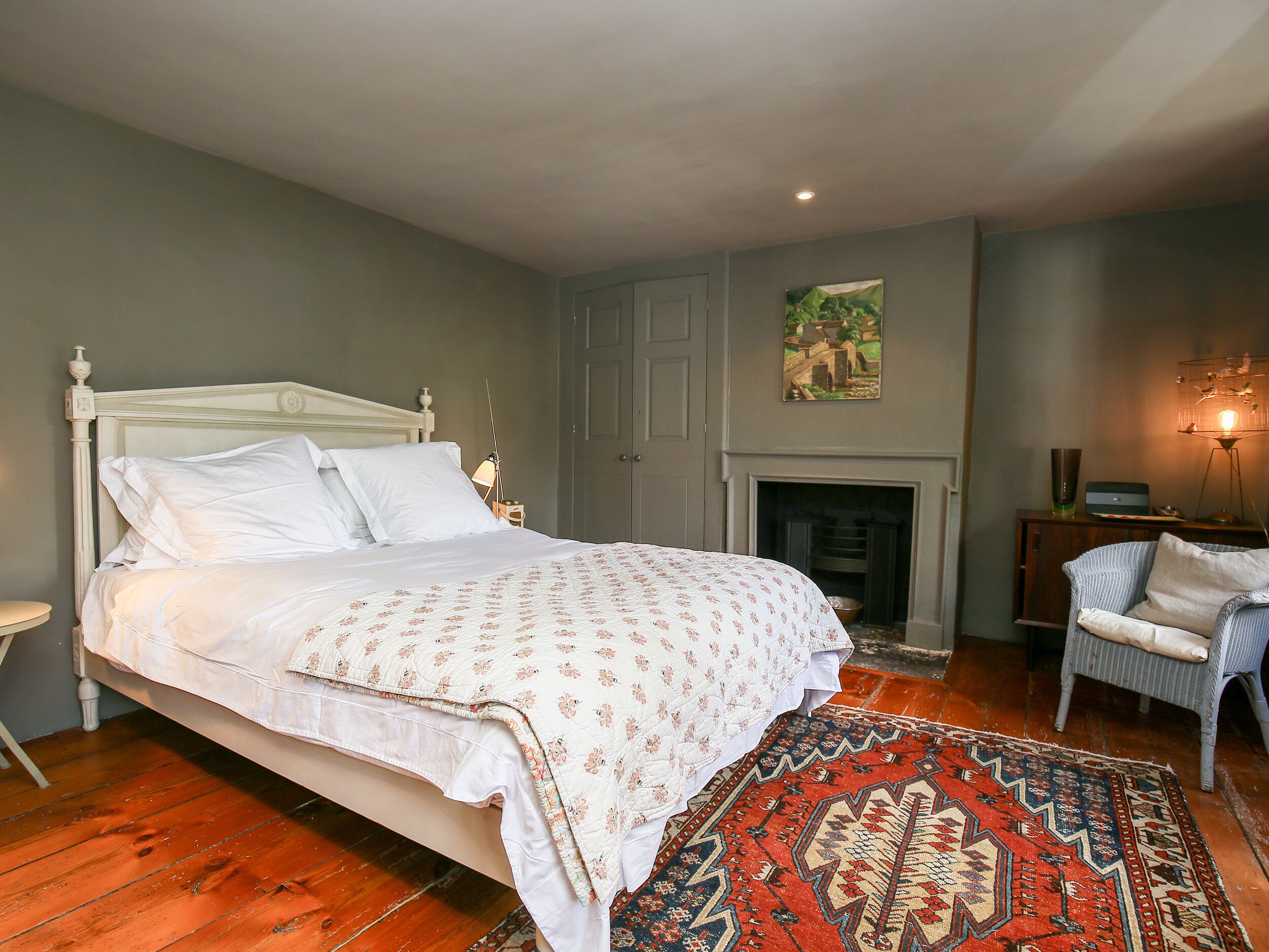A bedroom with a large bed, a fireplace, a chair, and a nightstand.