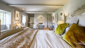 Une chambre à coucher avec un grand lit, une table de chevet, une commode, une coiffeuse avec un miroir et une fenêtre avec des rideaux.