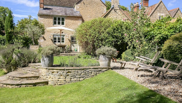 Une maison en pierre avec un jardin bien entretenu, une terrasse dotée de mobilier d’extérieur et un mur en pierre.