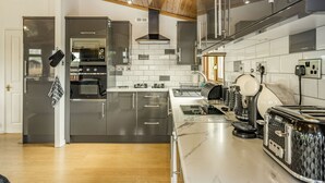 A modern kitchen with stainless steel appliances, a marble countertop, and wooden ceiling beams. - Lakeview Lodge (Carnforth)