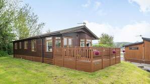 A wooden cabin with a fenced patio, large windows, and a view of the surrounding landscape. - Lakeview Lodge (Carnforth)