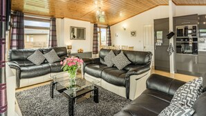 A living room with two leather sofas, a glass coffee table, and a kitchen area with stainless steel appliances. - Lakeview Lodge (Carnforth)