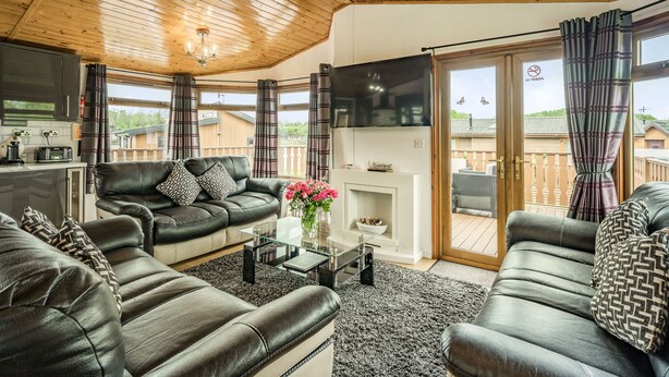 A modern living room with leather sofas, a glass coffee table, and a fireplace. - Lakeview Lodge (Carnforth)