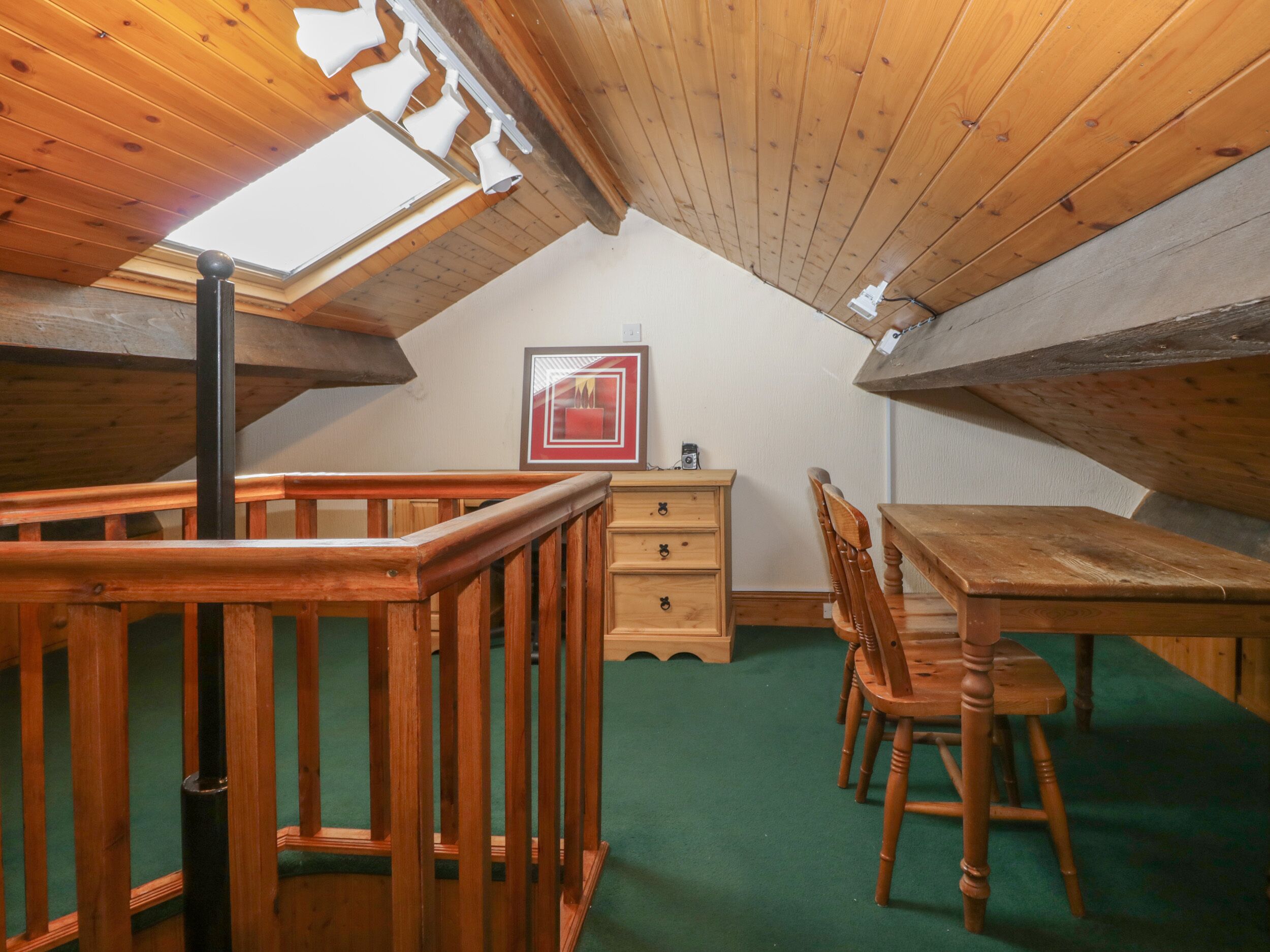 A cozy attic room with a wooden table and chairs, a dresser, and a framed picture on the wall.