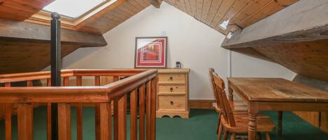 A cozy attic room with a wooden table and chairs, a dresser, and a framed picture on the wall.