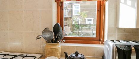Una cocina con estufa a gas, hervidor, dos tazas de té, una ventana con vistas al exterior y un tostador.