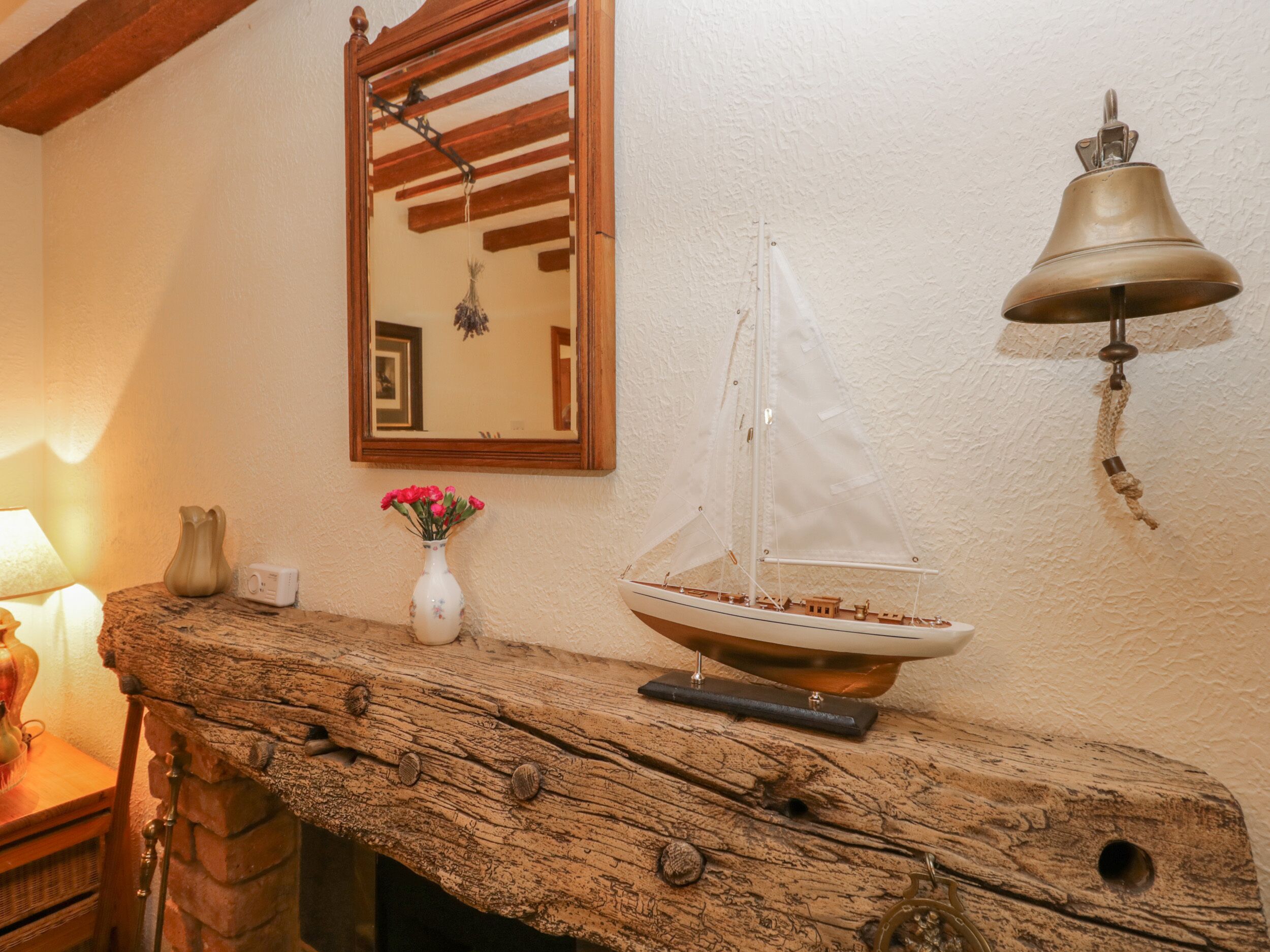 Un aparador de madera con un modelo de velero, un espejo, un timbre en la pared y un florero con flores.
