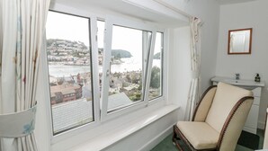 A room with a large window overlooking a harbor, a chair, and a small sink. - 21 Above Town (Dartmouth)