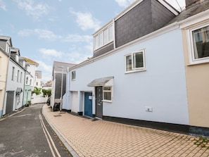 A narrow street lined with residential buildings, featuring a paved walkway and a blue door on the right. - 21 Above Town (Dartmouth)