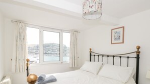 A bedroom with a bed, a window with curtains, a lamp, and a view of a harbor. - 21 Above Town (Dartmouth)