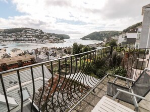 A balcony with a view of a coastal town, including houses, a harbor, and a hill in the background. - 21 Above Town (Dartmouth)