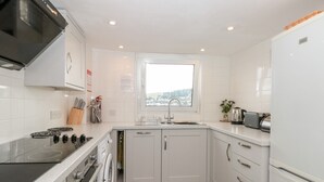 A modern kitchen with white cabinets, a built-in oven, a dishwasher, and a window providing a view. - 21 Above Town (Dartmouth)