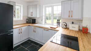 Een moderne keuken met witte kasten, een zwarte koelkast, een magnetron, een spoelbak en een houten aanrecht.