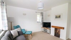 Een woonkamer met een grijze bank, smaragdgroene fauteuils, een televisie en een open haard.