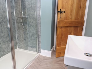 A bathroom with a glass shower enclosure, a wooden door, and a white sink.