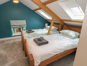 A room with a sloped ceiling, two wooden beds with leaf-patterned bedding, a window with a curtain, and a skylight.