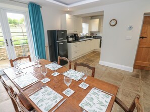 A dining area with a table set for four, a kitchen in the background, and a view of the outdoors through a glass door.