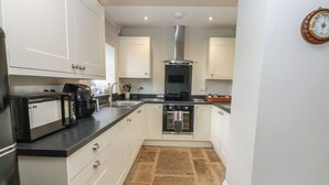 A kitchen with white cabinets, a black countertop, a built-in oven, and a stone-tiled floor. - White Lea (Richmond)