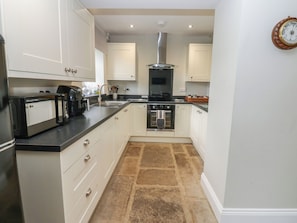 A kitchen with white cabinets, a black countertop, a built-in oven, and a stone-tiled floor.