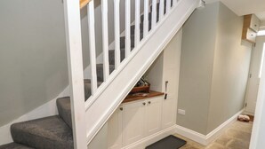 A staircase with a wooden handrail and white balusters, carpeted steps, a small wooden shelf, white cabinets, and a black doormat. - White Lea (Richmond)