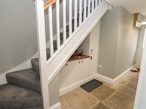 A staircase with a wooden handrail and white balusters, carpeted steps, a small wooden shelf, white cabinets, and a black doormat.