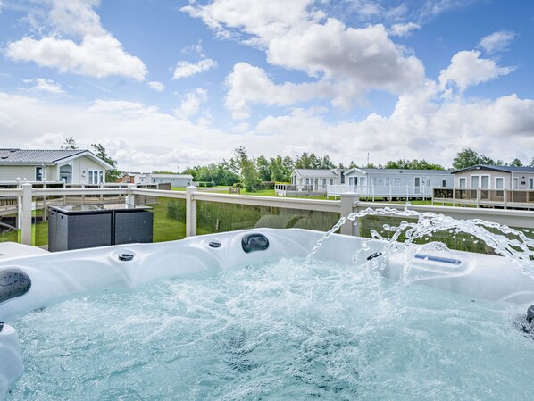 Un jacuzzi con agua salpicando, rodeado por una terraza y vistas a casas móviles al fondo.