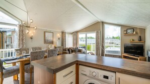 Eine moderne Küche mit integrierter Waschmaschine und Trockner, ein Essbereich mit Tisch und Stühlen sowie ein Wohnbereich mit Sofa und Fernseher.
